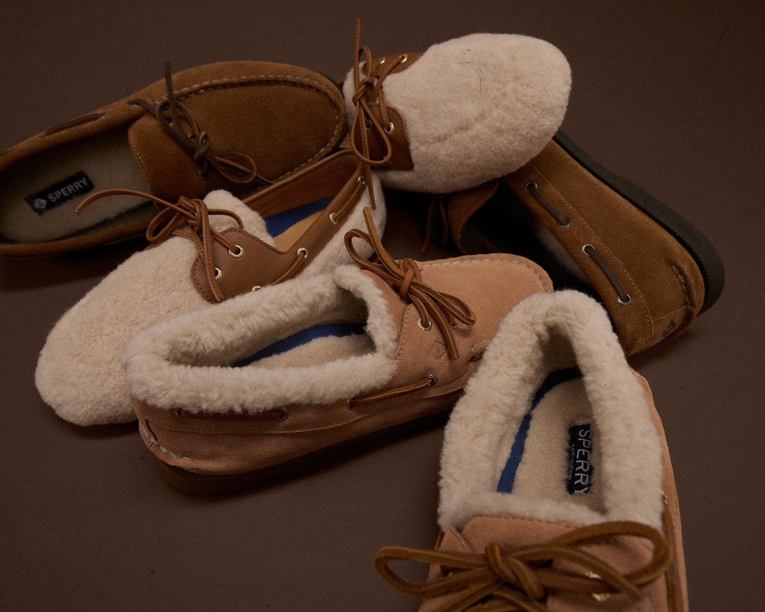 Three Sperry shearling-lined moccasins and boat shoes in tan suede, displayed on a dark surface
