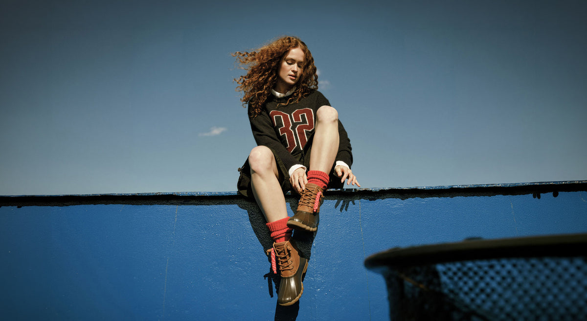 A woman sitting on a blue wall wearing a pair of tan duck boots