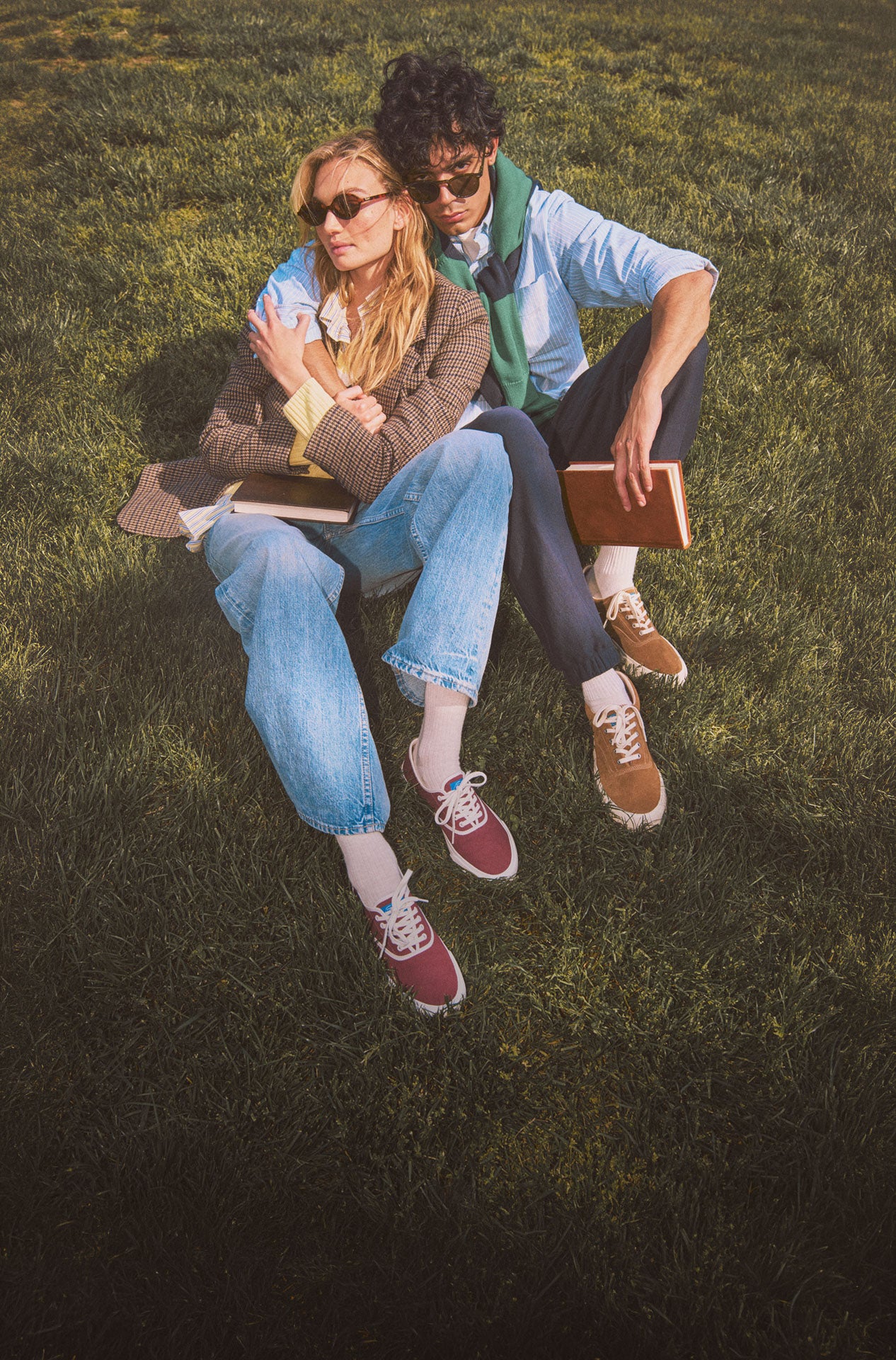 A man and a woman sitting on the grass holding books
