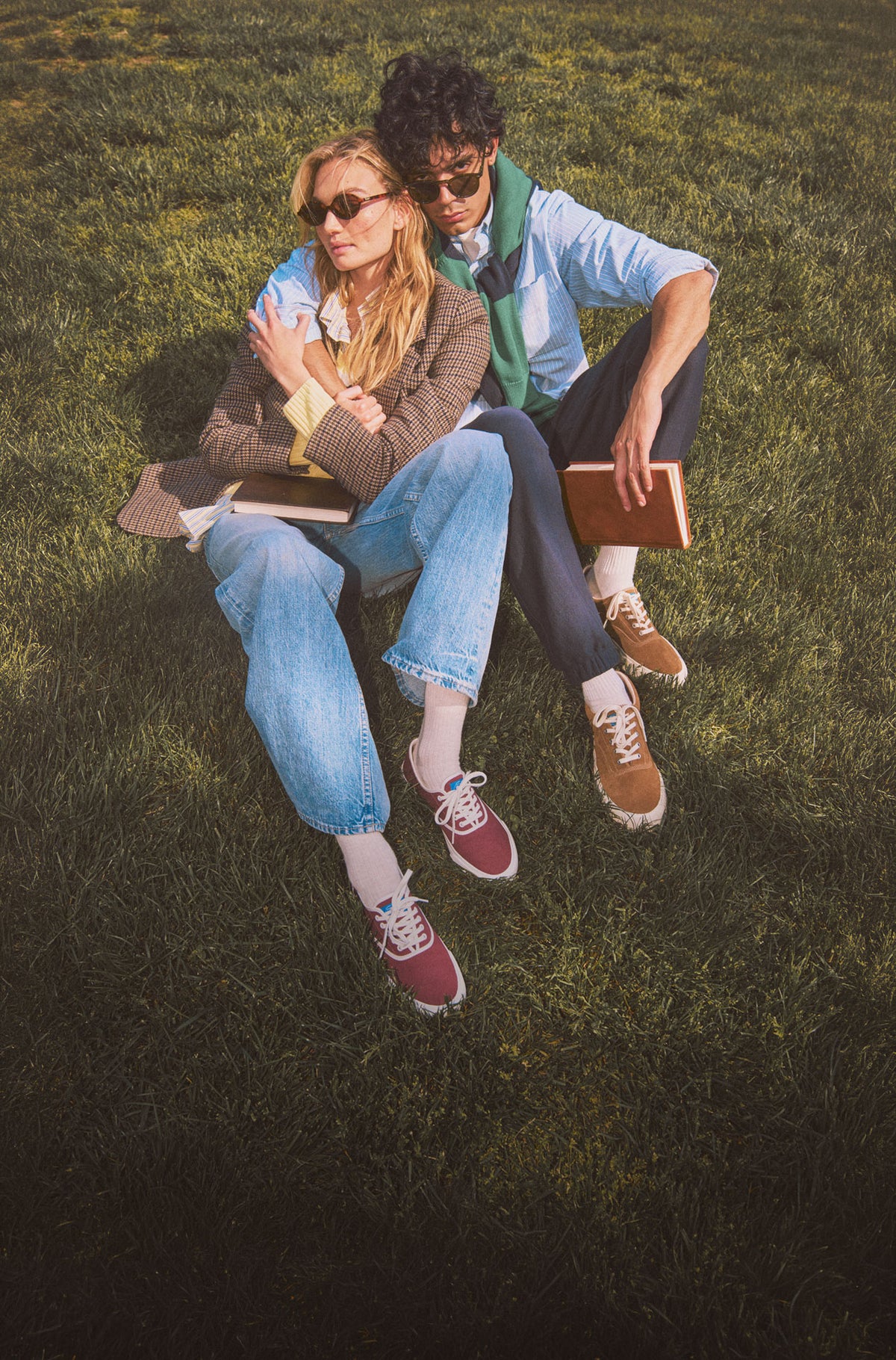 A man and a woman sitting on the grass holding books