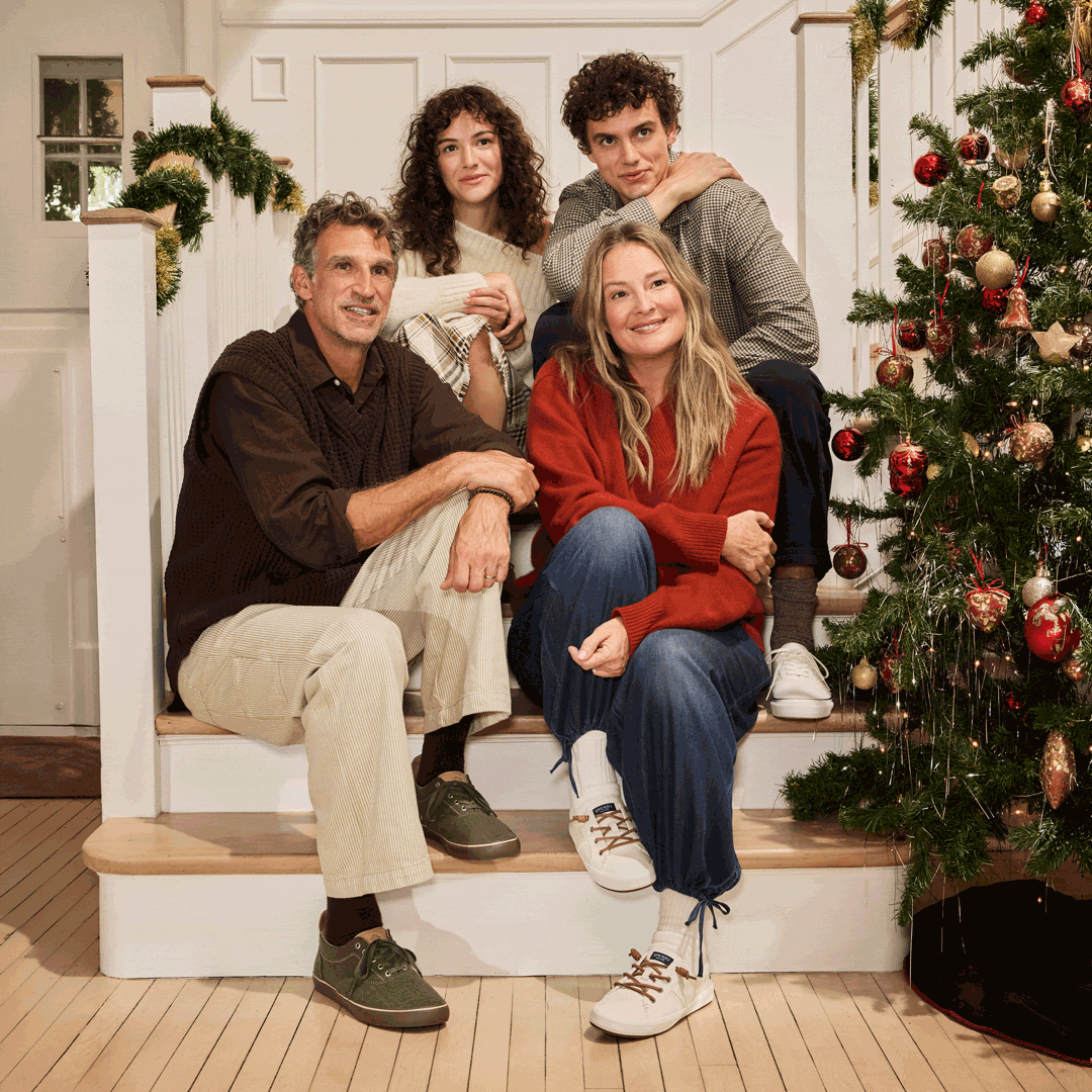 Animated GIF of a family of four on the stairs by a Christmas tree, shifting from all looking aside to the parents facing each other while the siblings look at the camera.