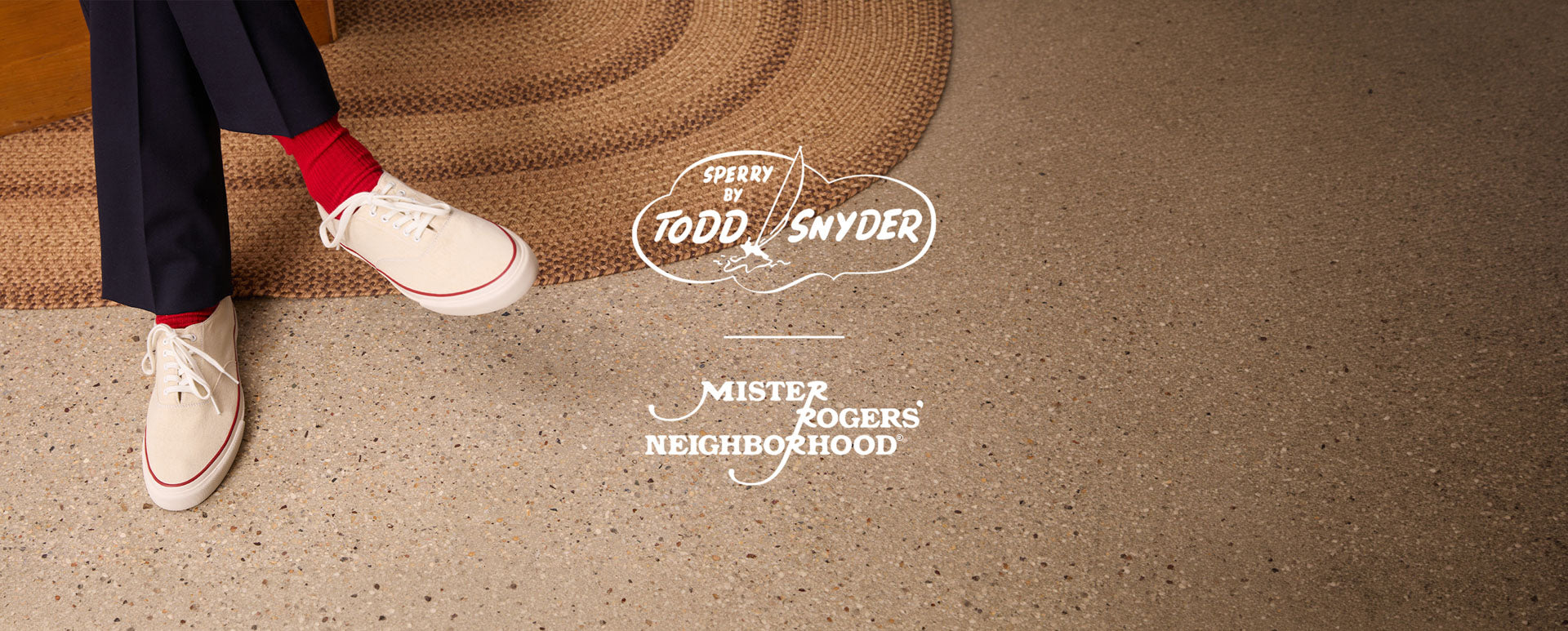 Person in navy trousers and red socks wearing white Sperry x Todd Snyder CVO canvas sneakers with red accent stitching, seated beside a braided rug on a terrazzo floor, with Sperry by Todd Snyder and Mister Rogers' Neighborhood logos overlaid.