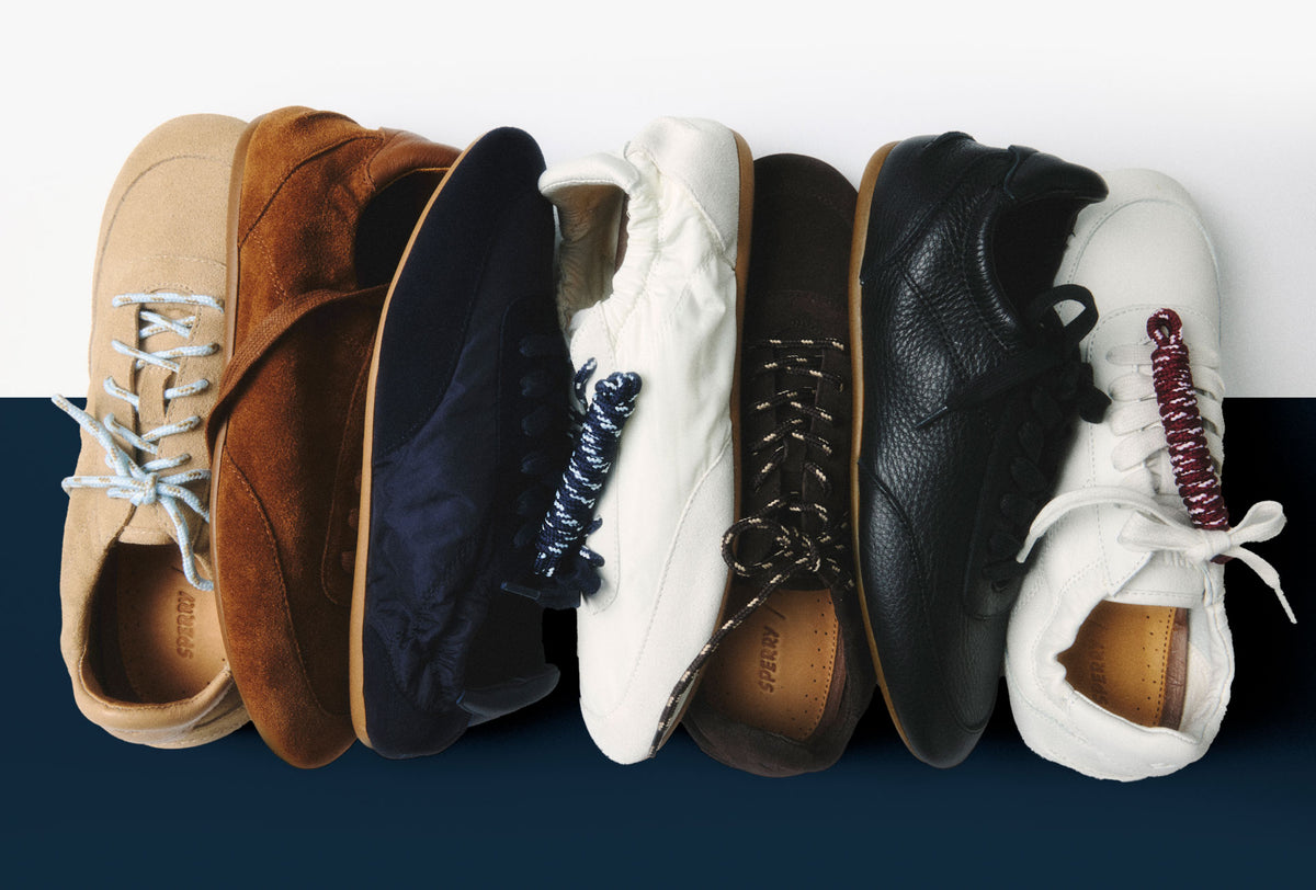 Flat-lay of six Sperry x Aritzia sneakers lined up side by side, showing the full colorway range: tan suede, brown suede, navy, white, black leather, and white leather with burgundy braided lace detail.