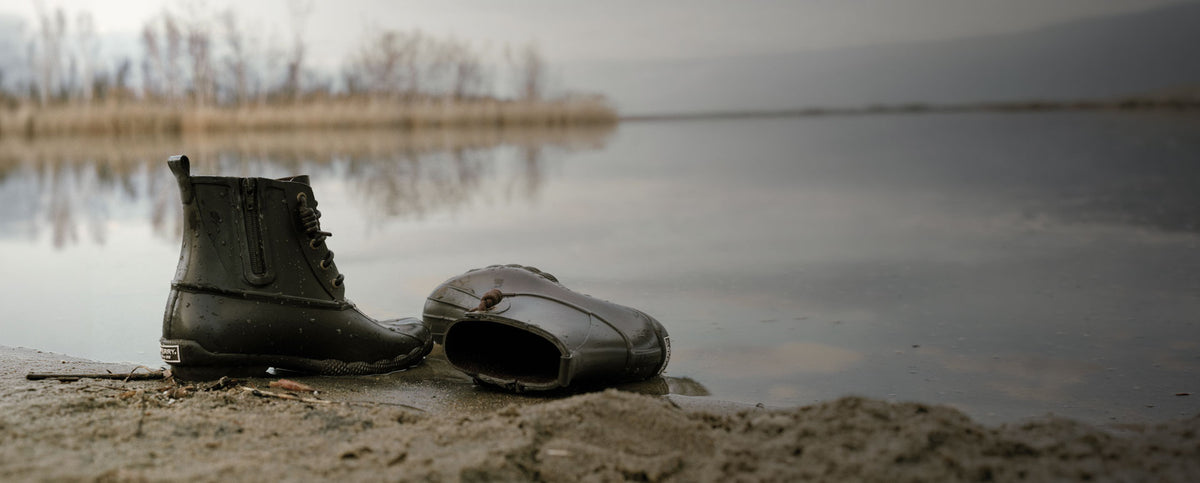 A pair of brown rubber duck boots by the water
