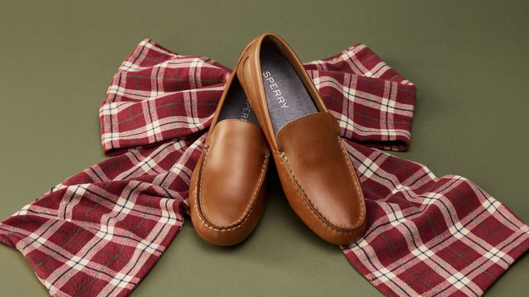 Man in a tropical print shirt and dark trousers seated on a green velvet chair wearing cognac leather penny loafers, alongside a close-up of the shoe with grey dress socks.