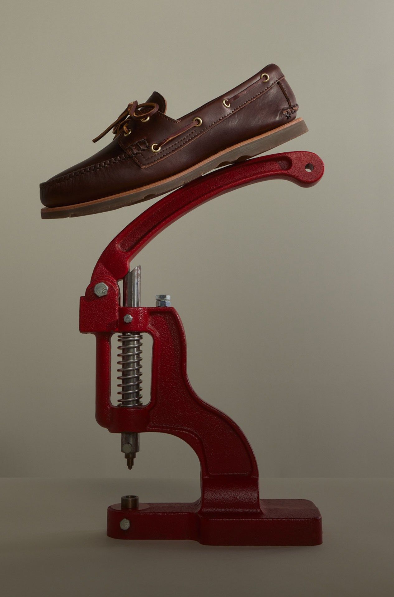 White Sperry Gold Cup leather boat shoe suspended in mid-air surrounded by floating cobbler tools — a hammer, pliers, caliper, and lasting pincers — against a grey background, highlighting the handcrafted construction process.