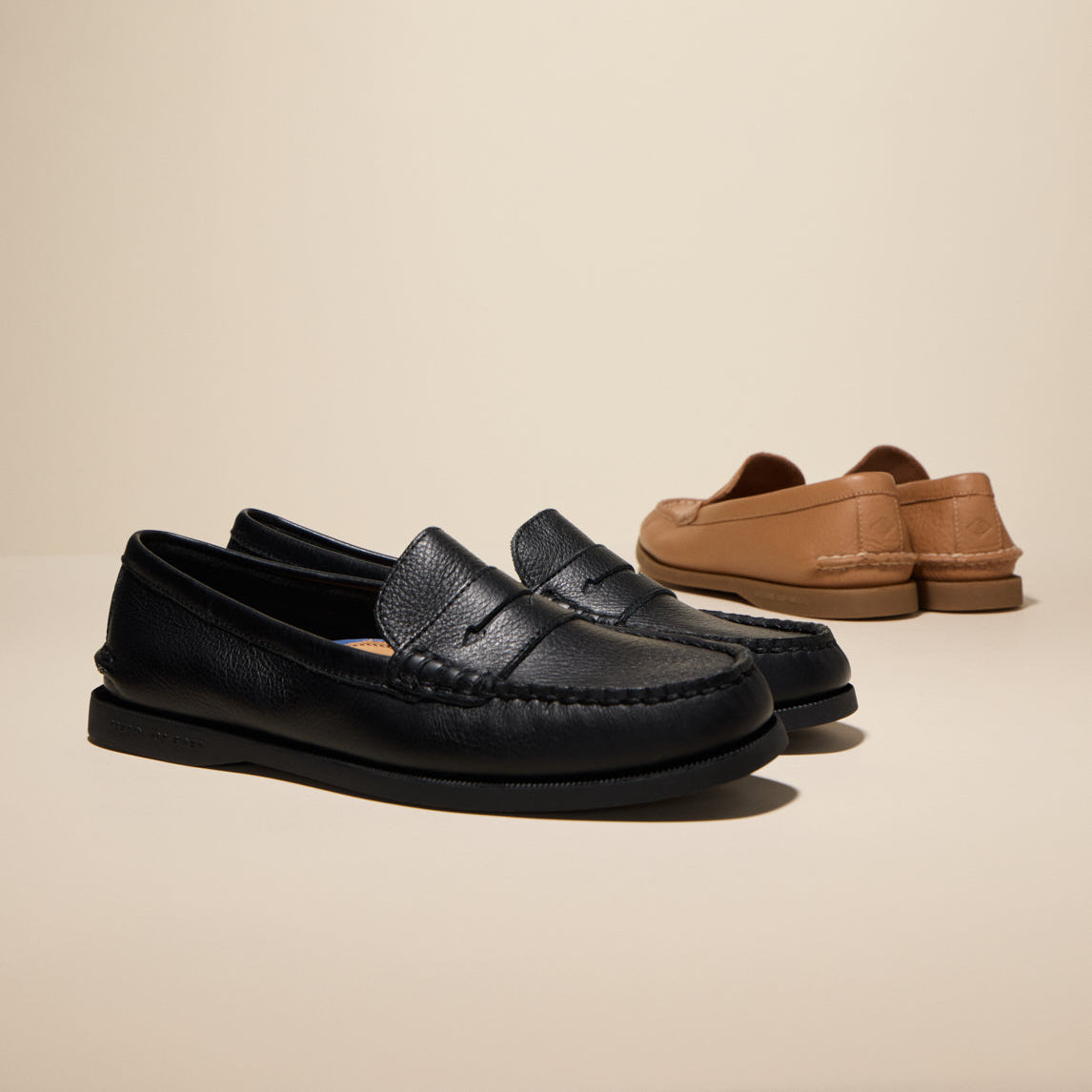 Two pairs of black and brown loafers against a beige background