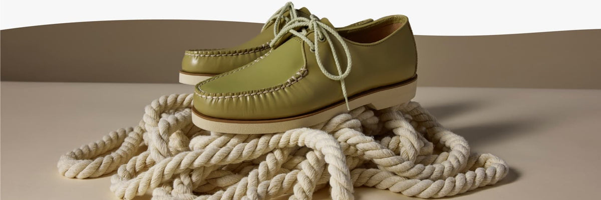 Sage green leather Sperry moccasin-style shoes with rope lacing and hand-stitched welt, displayed on a coil of thick nautical rope against a neutral background.