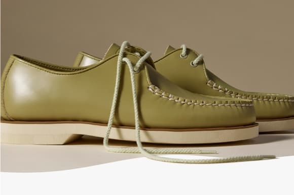 Pair of sage green leather moccasin-style shoes with rope lacing, hand-stitched welt detail, and a cream rubber sole, displayed on a neutral background.