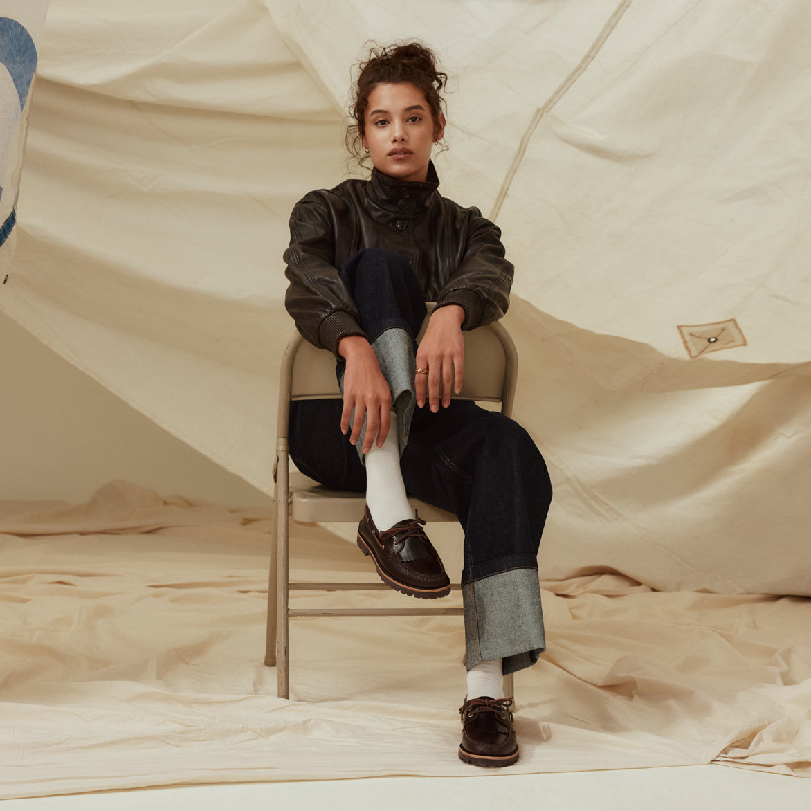A woman sitting on a backwards beige foldable chair wearing a pair of brown boat shoes