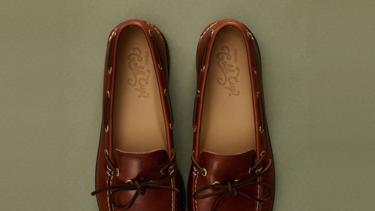 Paire de chaussures bateau Sperry Gold Cup en cuir bleu marine avec lacets camel et surpiqûres contrastantes, posée sur une chaise en métal turquoise vieilli.